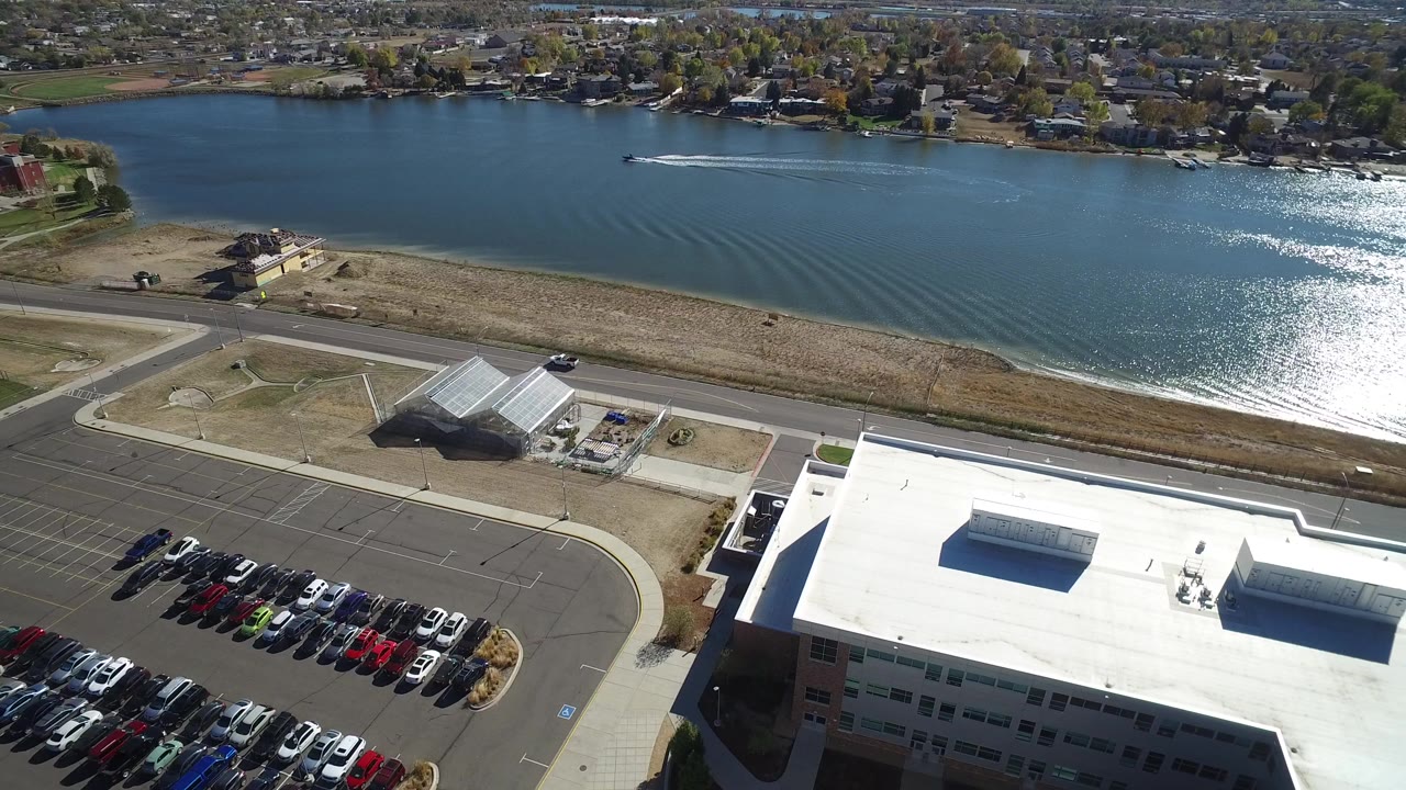 Aerial view of a lakeside building, parking lot, road, and blue water.