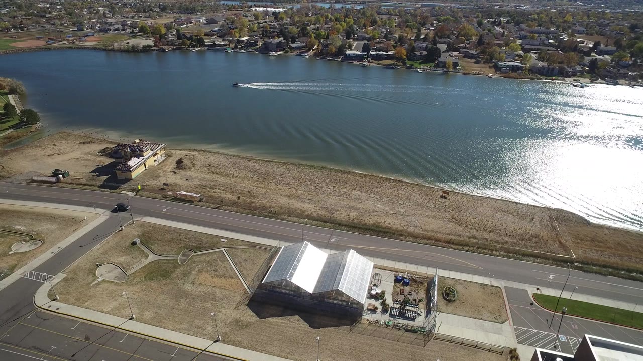 Drone-style view of a lake with a motorboat, ripples, shoreline homes, and a road.