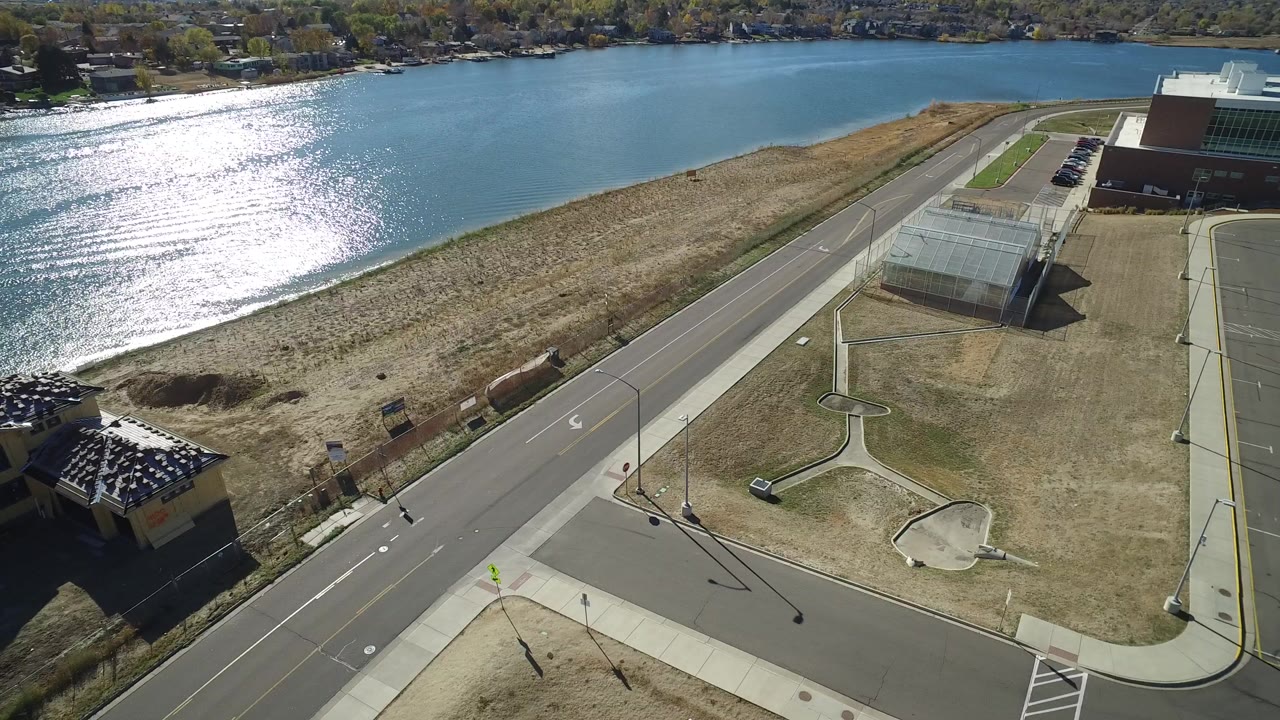 Aerial view of a lakeside road, shoreline grass, buildings, and bright water glare.