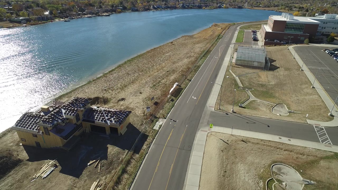 Aerial view in Hidden Lake, Colorado, showing the lake filling the upper frame, a sandy strip along the water, the foreground house, a road intersection, sidewalks, and no visible people.