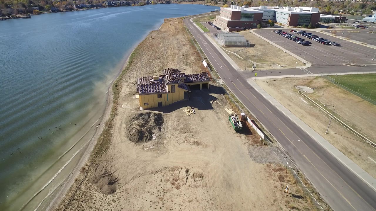 Aerial view of sandy lakeshore, construction site, road, and large buildings beside blue water.