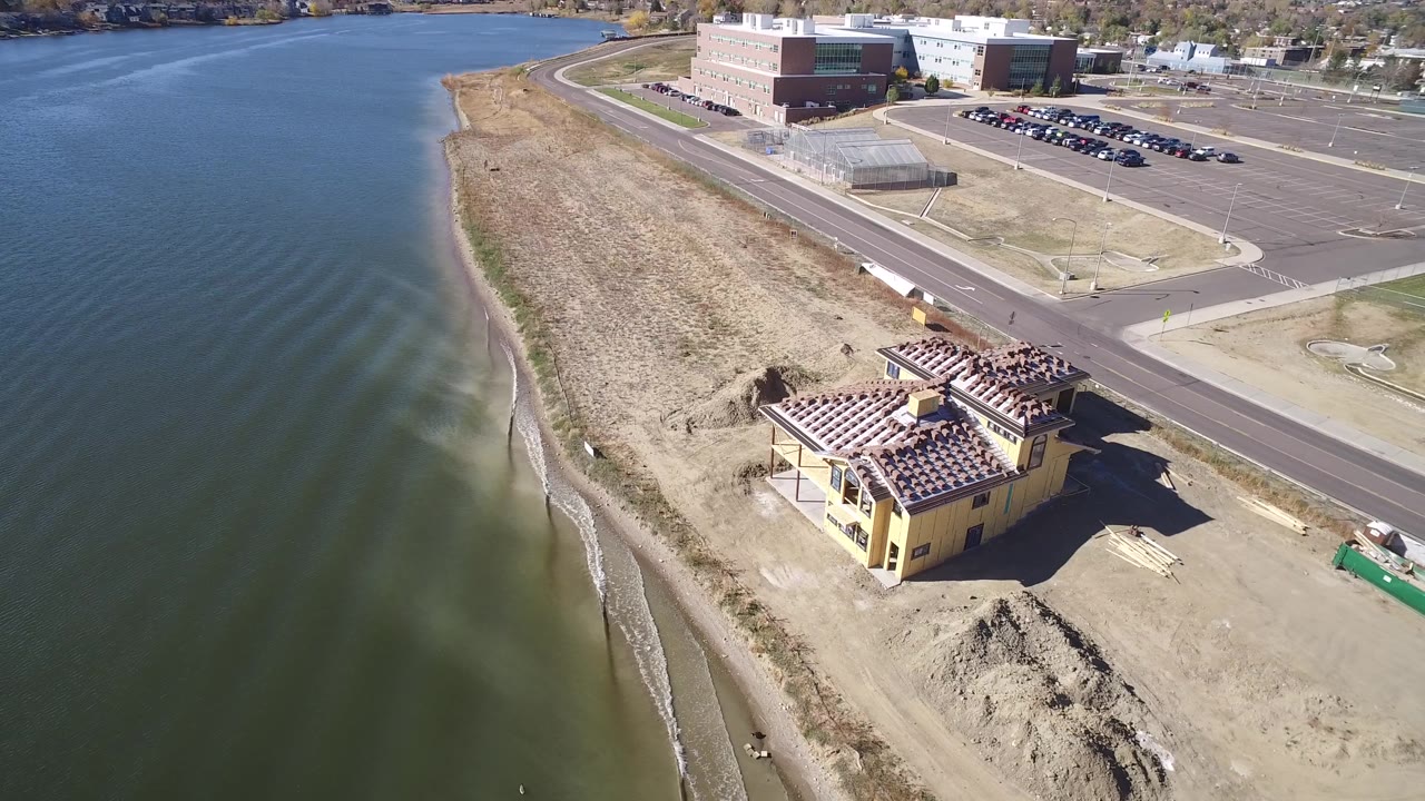 High angled aerial view of small waves along shore with a construction site and parking lots beyond.