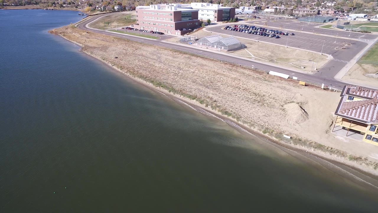 Oblique aerial of a lake shoreline with buildings, roads, and parked cars inland.