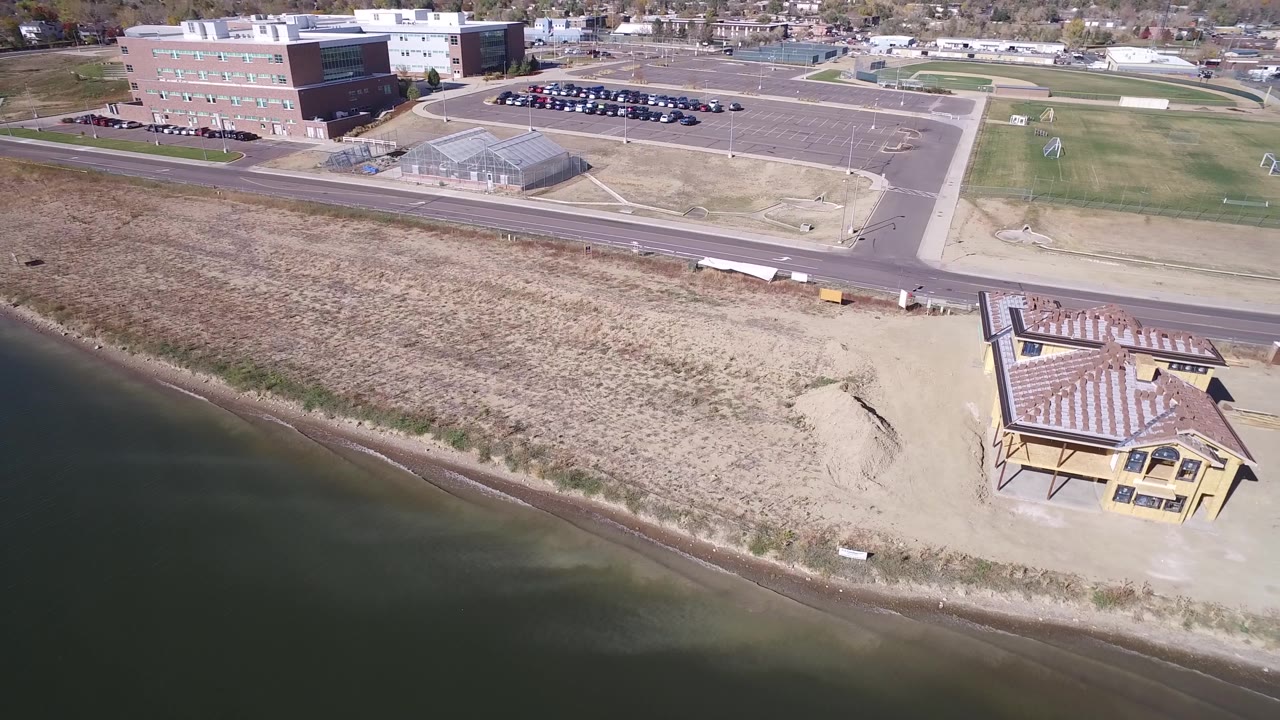 Drone-style view of a beachside building beside calm lake water and dry grass.