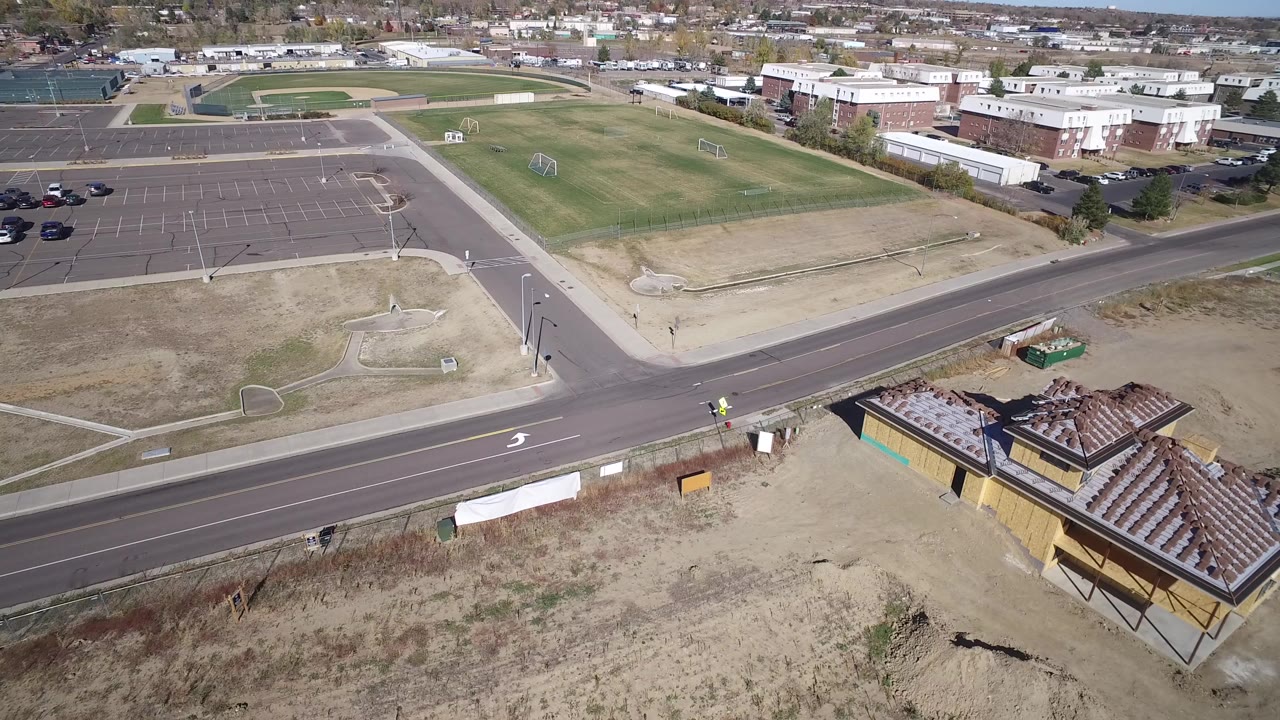 Elevated view of a road intersection, open field, parking lot, and low buildings.