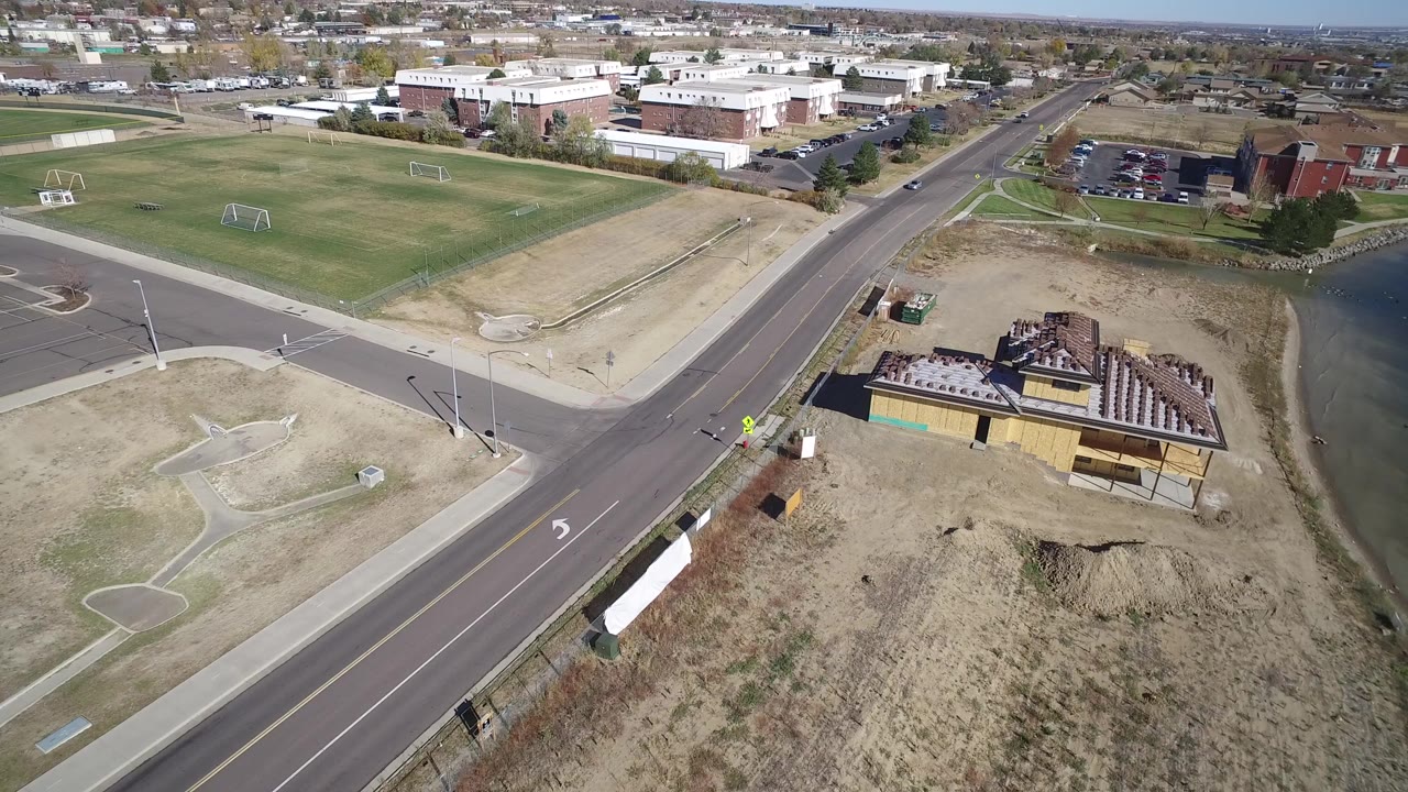 Aerial view of a road, sports fields, buildings, dry lots, and lake edge.