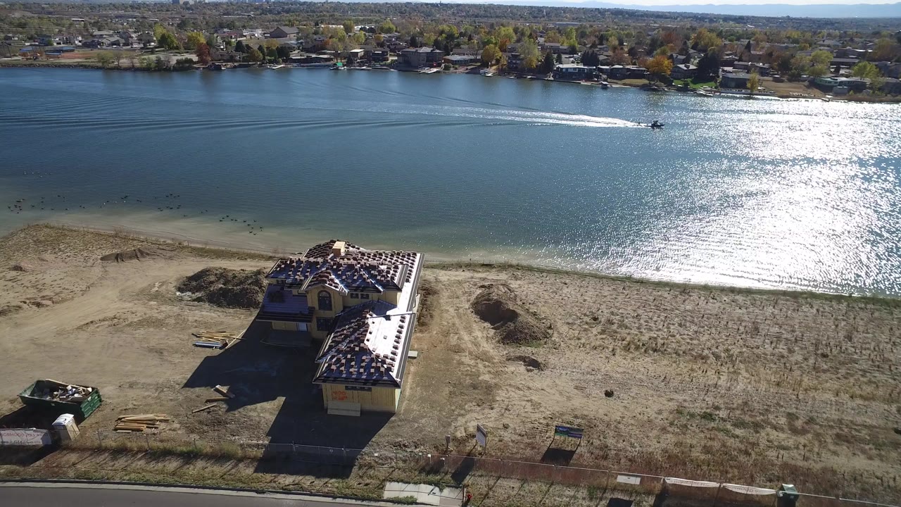 Aerial view of a blue lake, dry shoreline, and a roadside building