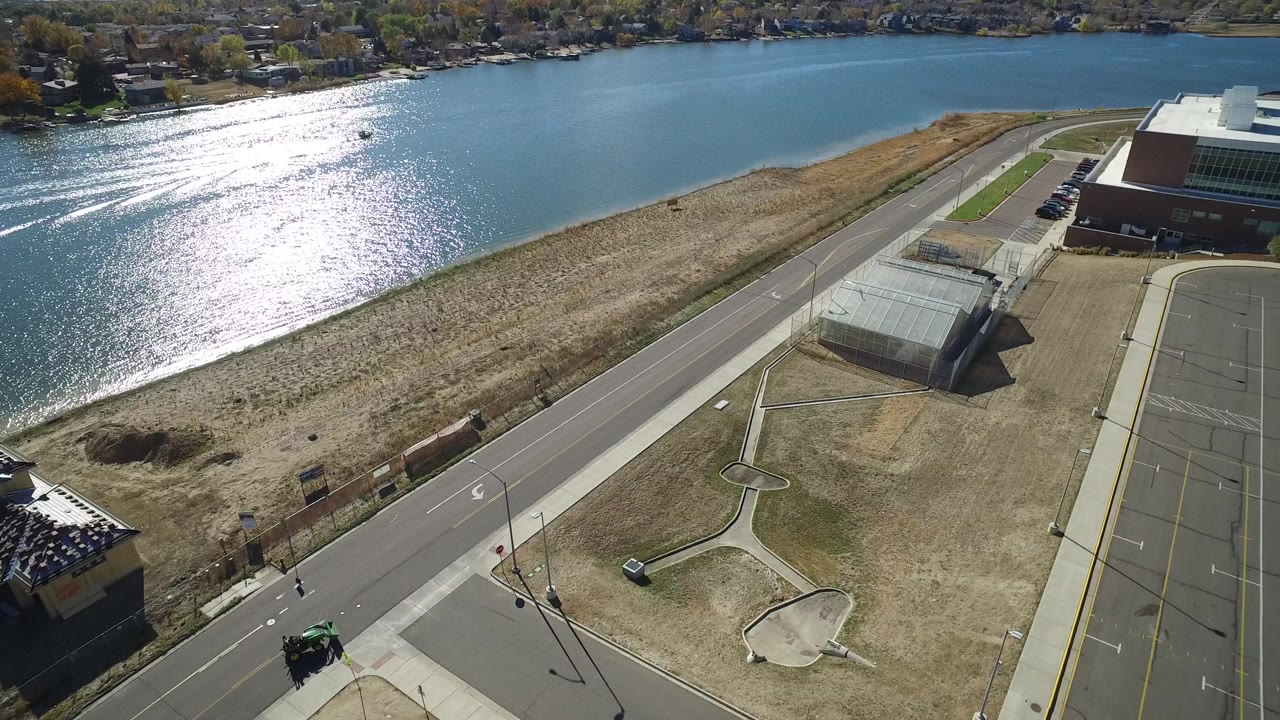 Aerial view of a blue waterway, road, shoreline grass, and building parking area.