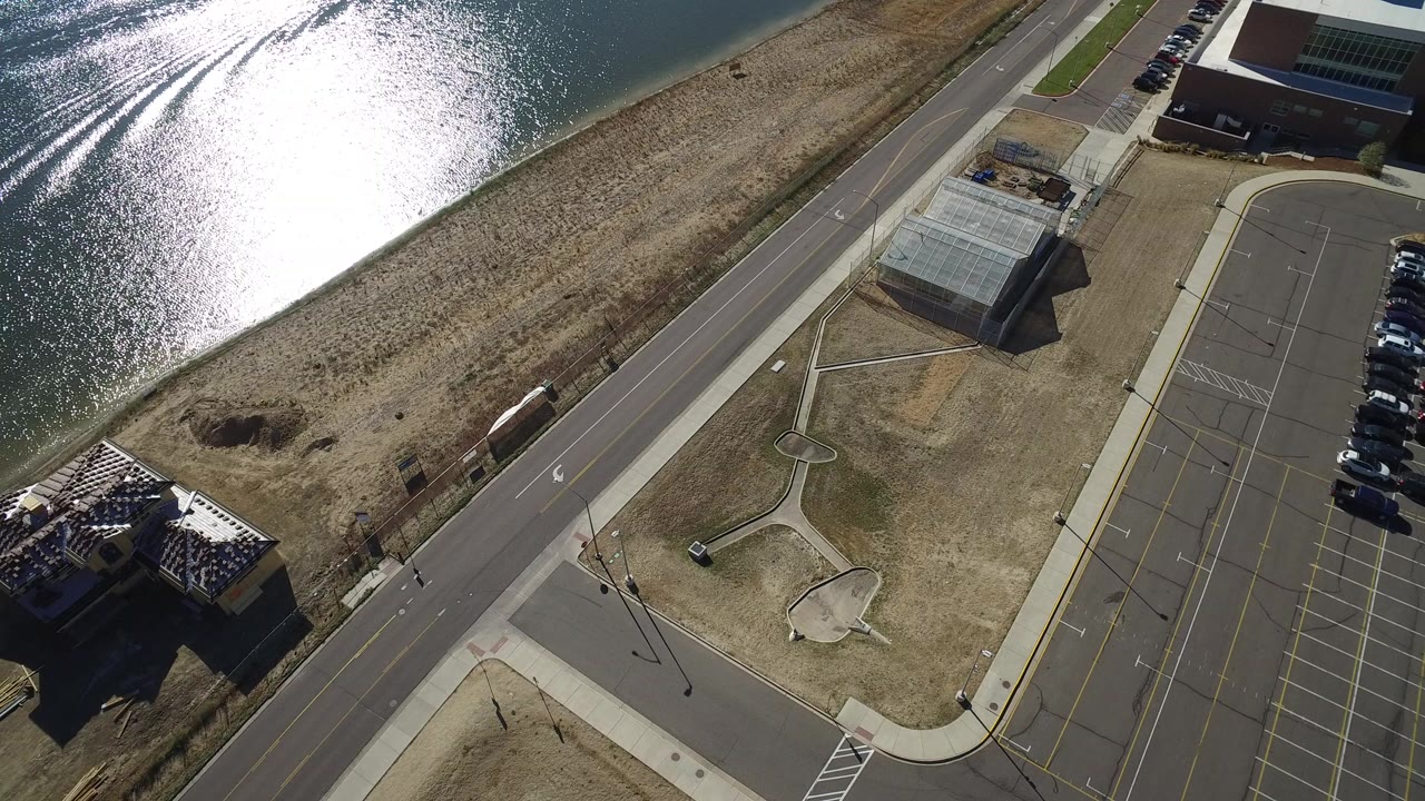 Aerial view of lake glare, road, parking lot, and low buildings.