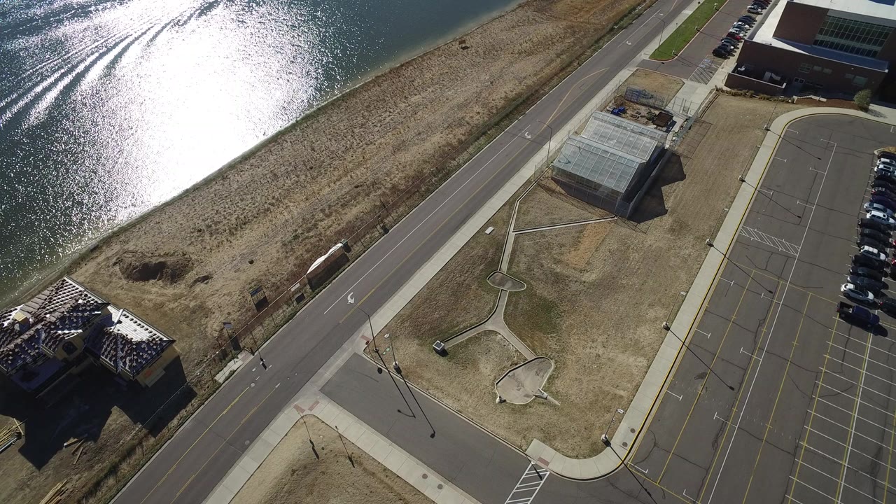 Aerial view over Hidden Lake, Colorado with intense reflection on the water, a road cutting through dry grass, and a mostly empty parking area beside low buildings.