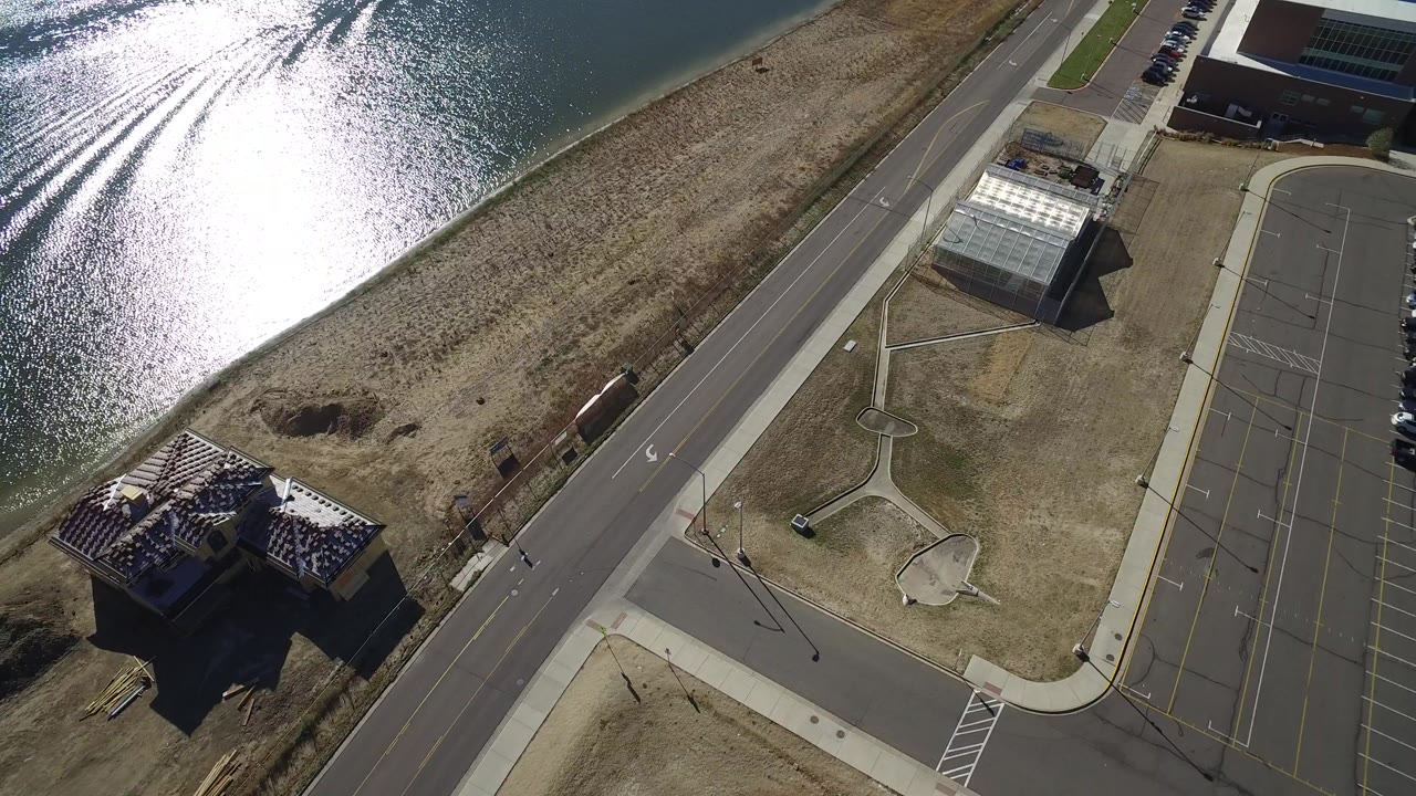Aerial view of lake glare, shoreline, road, and nearby buildings.