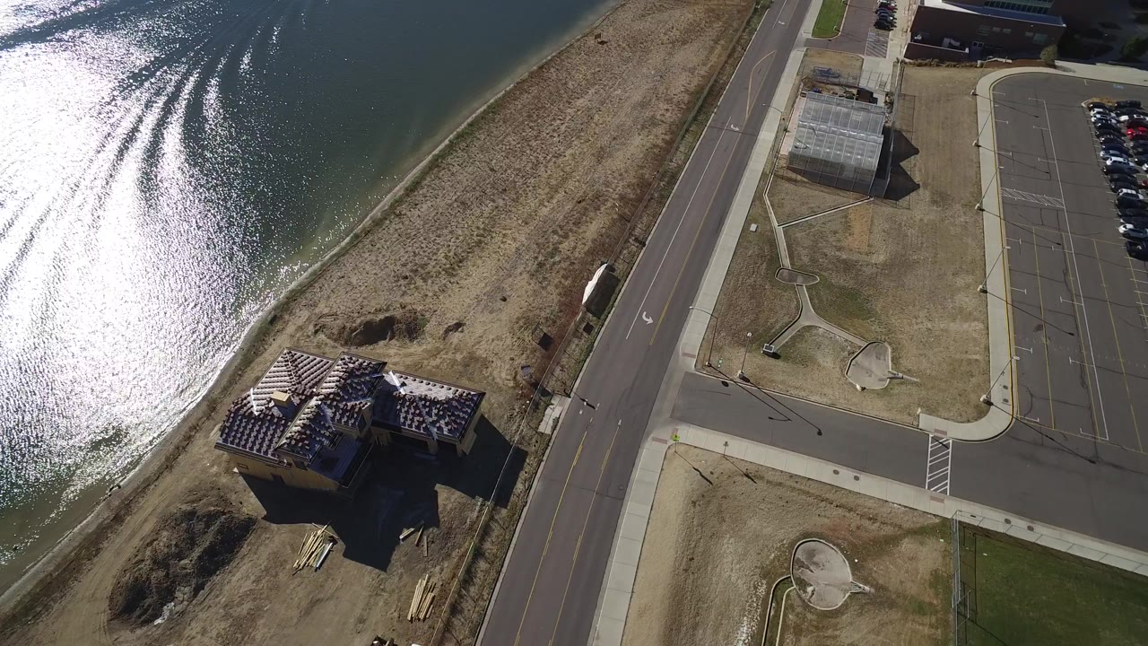Aerial view of lake water, shoreline, road, small buildings, and parking lot.