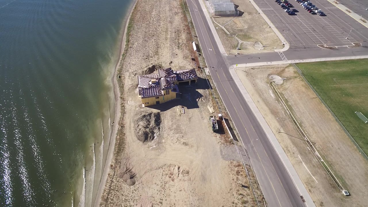 Aerial view of shoreline, house, road, parking lot, and water.