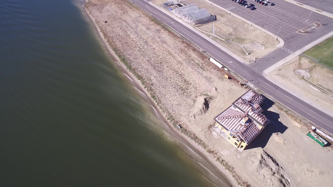 Aerial view of lake shoreline, road, parking lot, and yellow house.