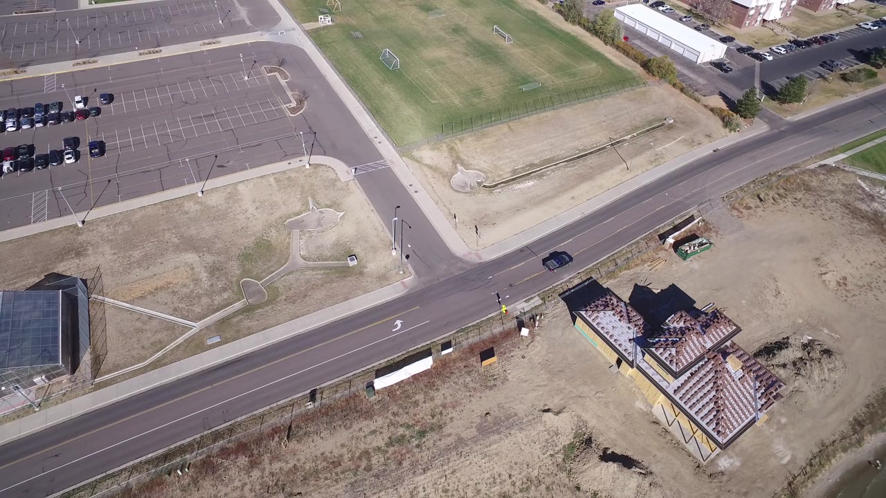 High aerial view in Hidden Lake, Colorado showing a road crossing between parking lots, dry open ground, green fields, a house near the water, and no visible people.