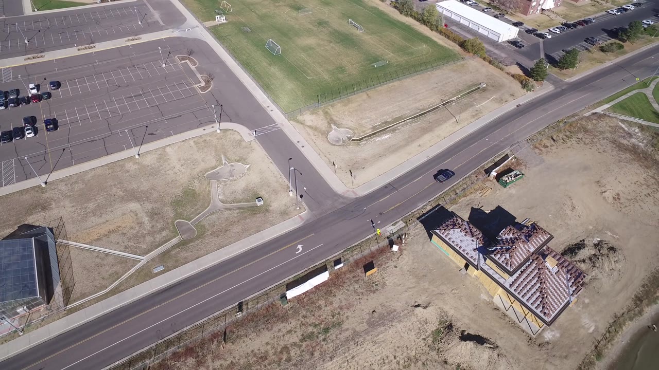 Road and parking lot seen from above with homes and water nearby.