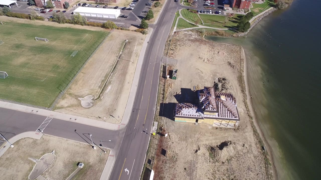 Overhead road, open land, lakeshore, and roof-framed building.