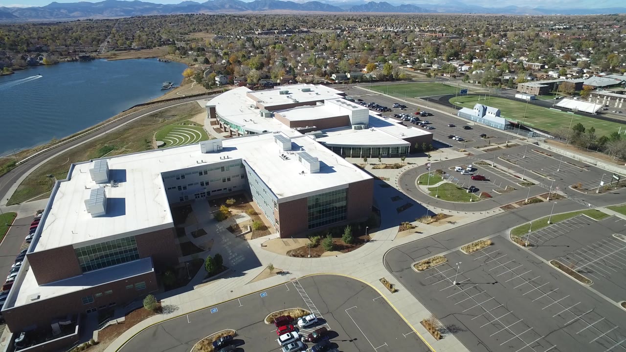 High aerial of commercial buildings, empty parking lot, lake, and town beyond.