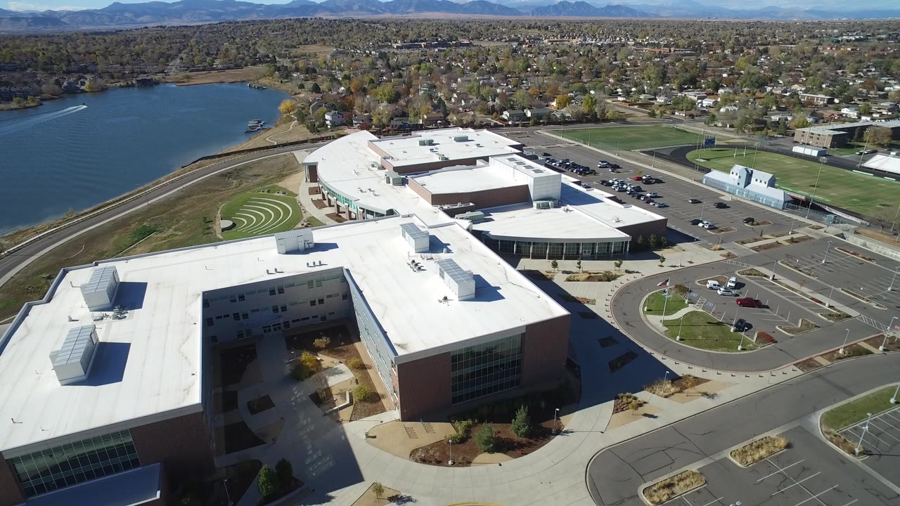 Aerial view of white-roofed commercial buildings beside a lake and parking lot.