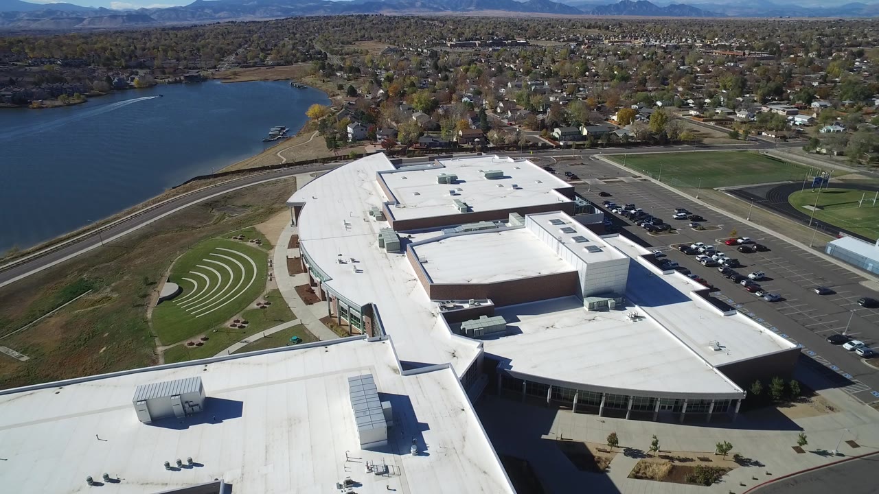 Wide drone frame of a building complex with lake on the left and fields on the right.