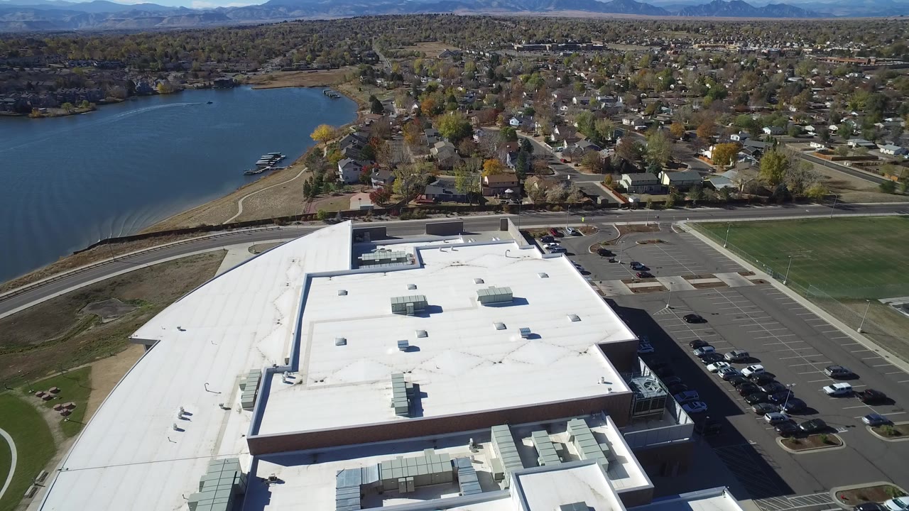 Aerial view of a white flat-roofed building beside a lake and neighborhood