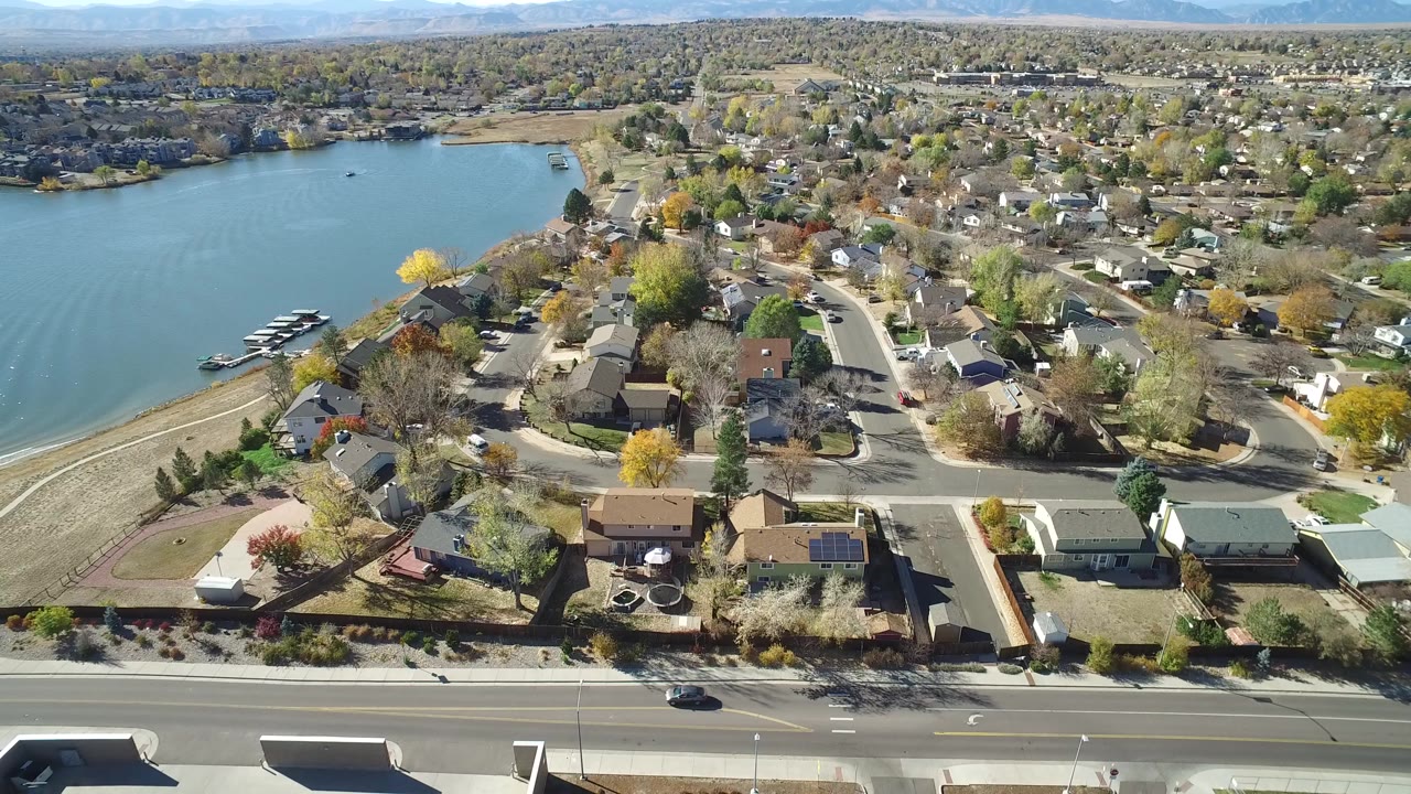 Aerial view over Hidden Lake, Colorado with the lake on the left, residential streets and homes in the center, a wide road in the foreground, and no visible people.