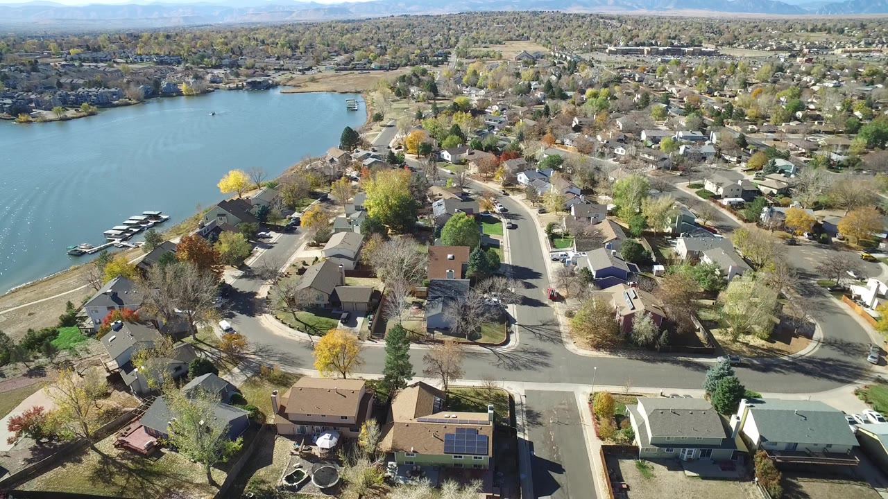 Opening aerial frame over Hidden Lake, Colorado, showing the lake on the left, docks near shore, curving streets, private homes, and trees in bright daylight.