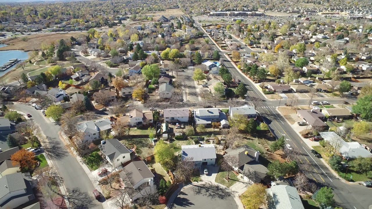 Aerial view of residential streets, houses, trees, and a small lake edge.