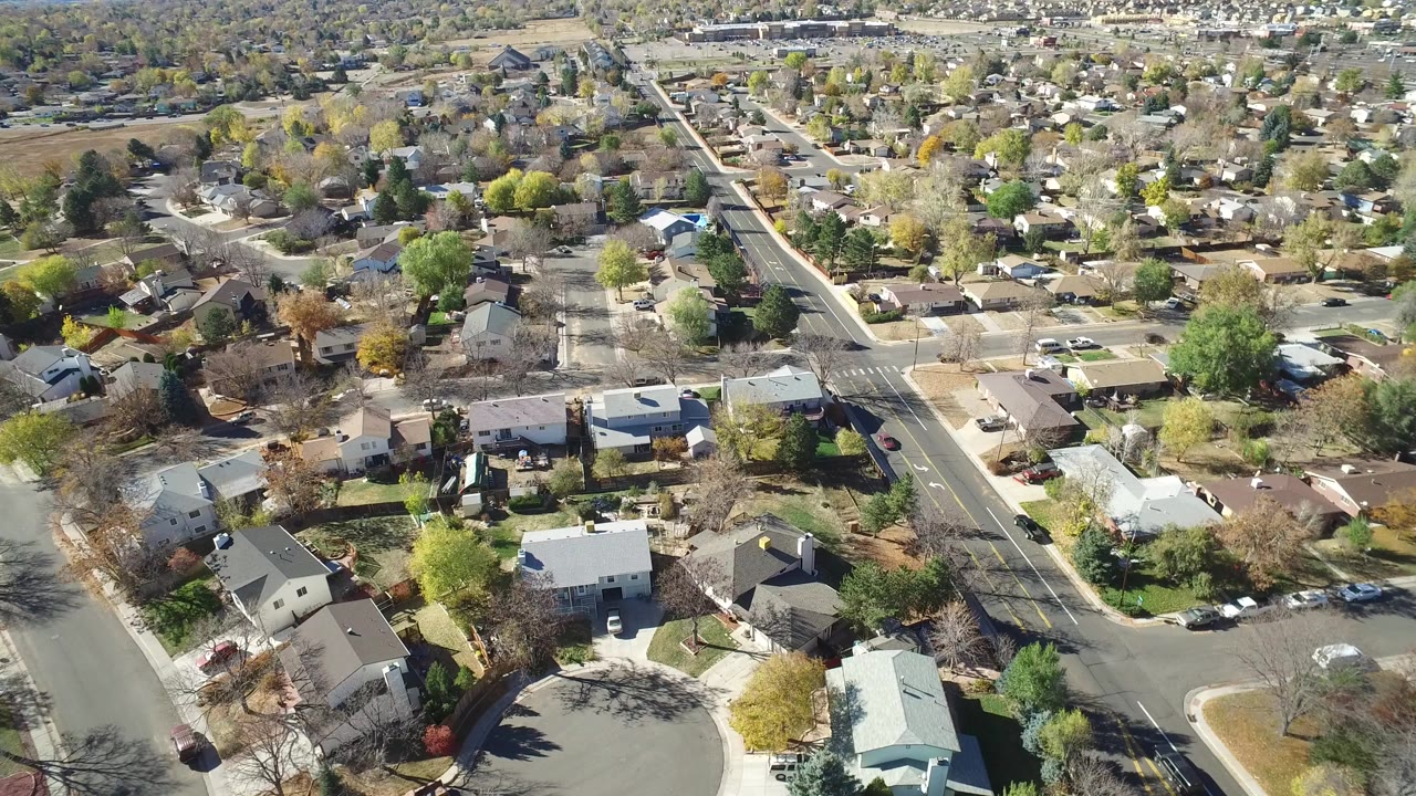 Elevated aerial view over Hidden Lake, Colorado homes and neighborhood roads, with autumn-colored trees, parked cars, and no visible people.