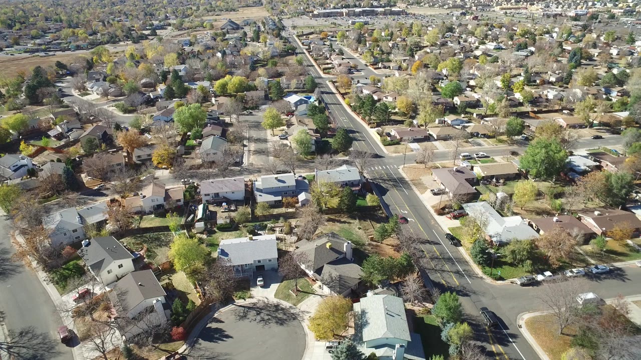 Drone-style view of homes and tree-lined streets in bright sun.