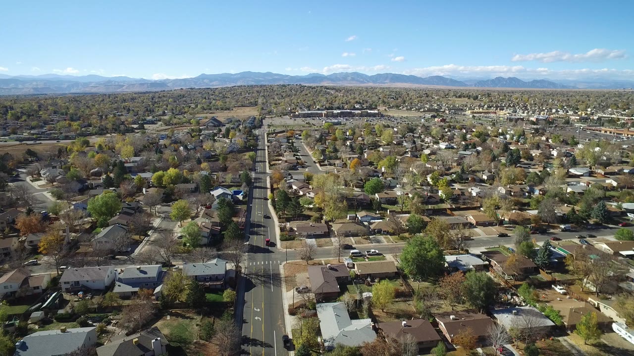 Aerial view over houses, streets, trees, and distant mountains.