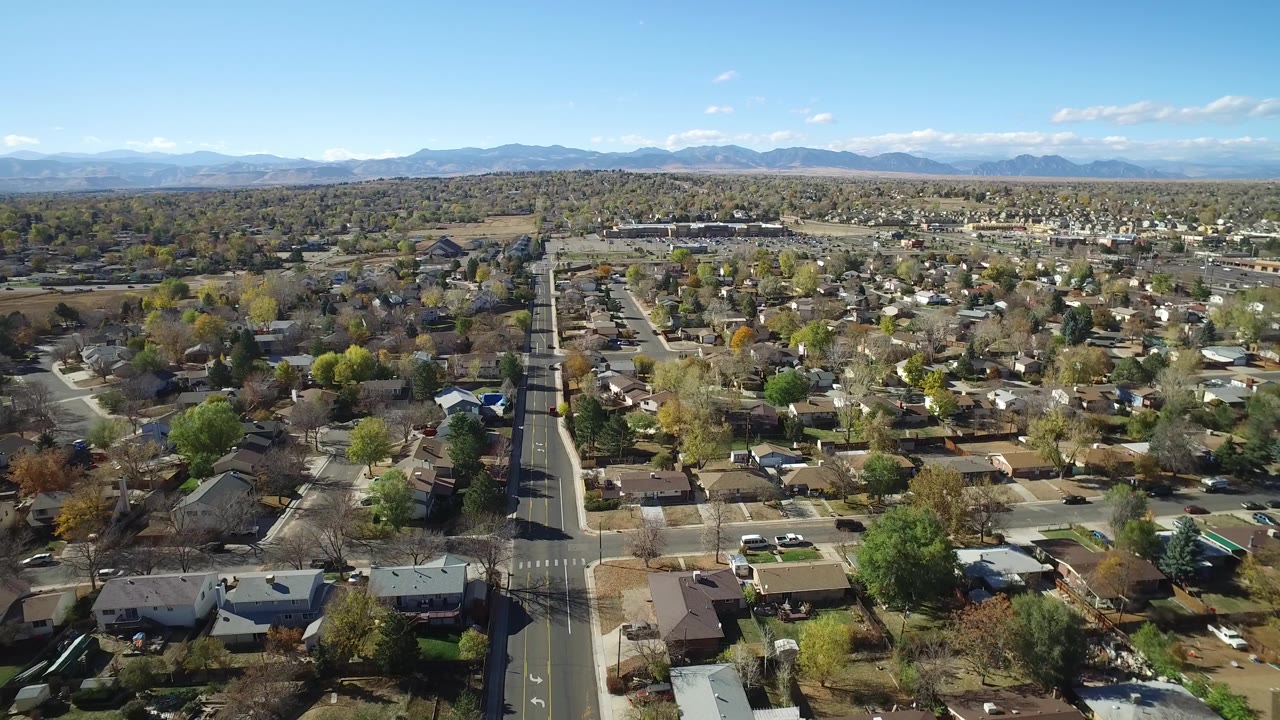 Aerial view of a suburban neighborhood with roads, houses, trees, and distant mountains.