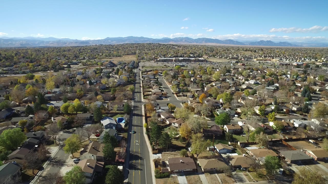 Aerial view of suburban houses, a straight road, trees, and distant mountains.