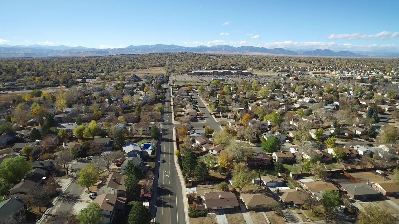 Elevated view of Hidden Lake, Colorado showing dense residential blocks, a straight road near the center, scattered trees, distant mountains, bright sky, and no visible people.