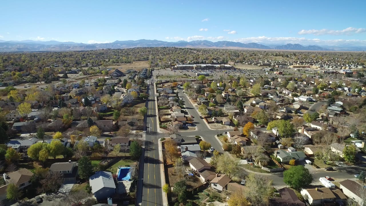 Aerial view over suburban houses, streets, trees, and distant mountains.