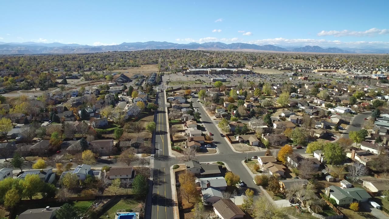 Opening aerial frame over Hidden Lake, Colorado, showing residential streets, single-family homes, autumn-toned trees, distant mountains, blue sky, and no visible people.