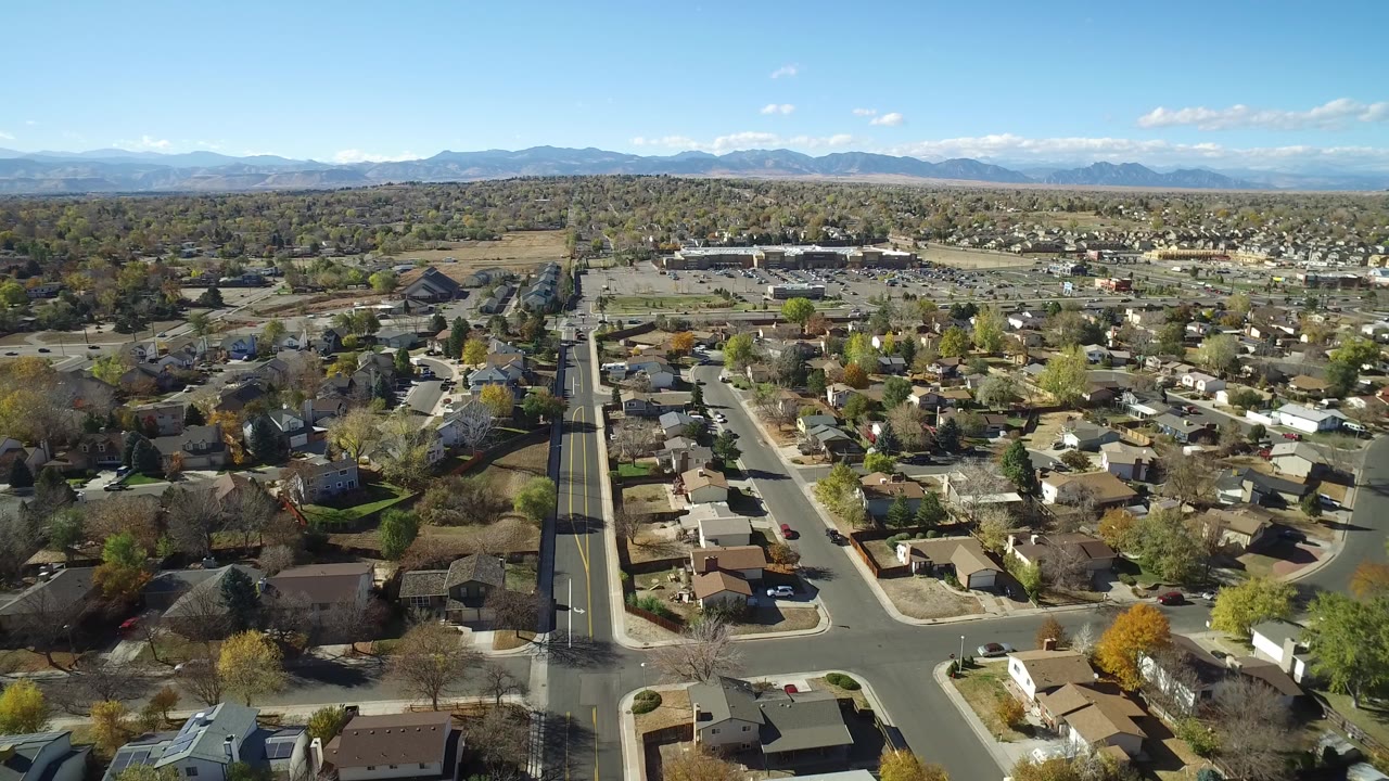 Aerial view over suburban houses, roads, trees, and distant mountains.