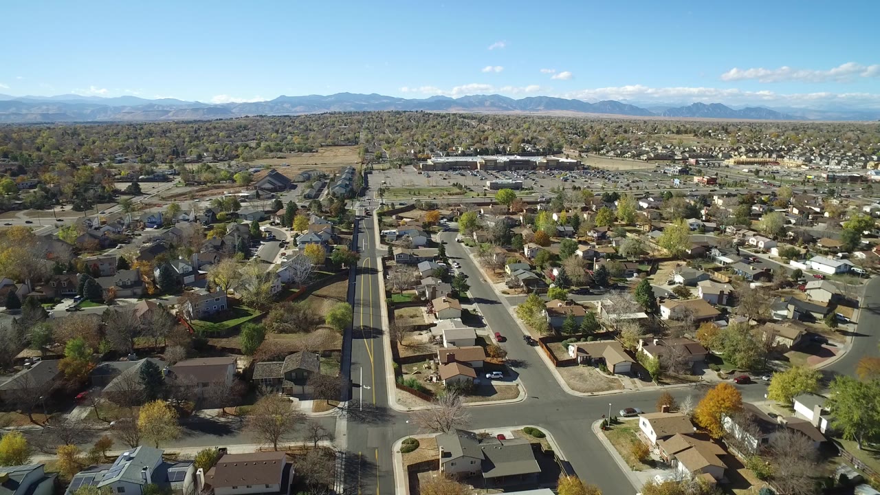 Hidden Lake, Colorado appears from above with the central road extending toward the horizon, rooftops and yards on both sides, light traffic, and no visible people.