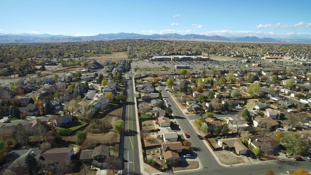 Aerial view over suburban houses, streets, trees, and distant mountains.