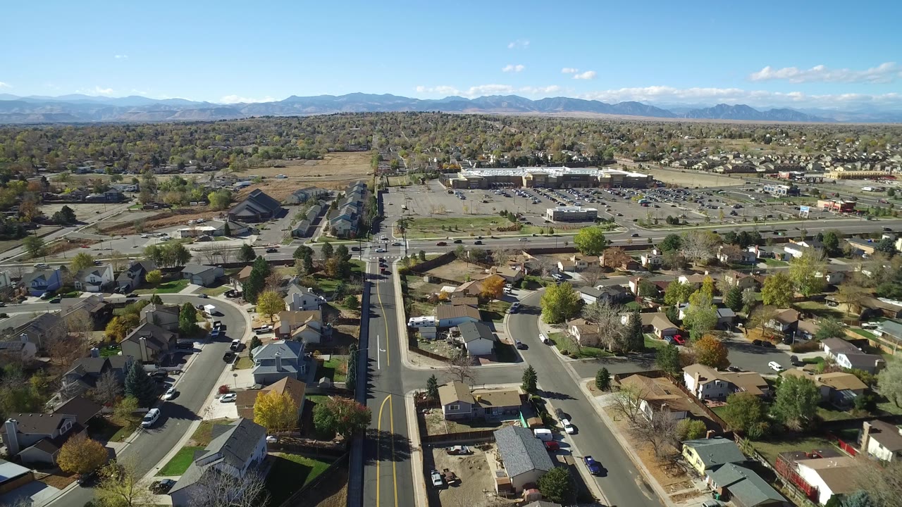 Drone-style view across homes, neighborhood streets, parking lots, and a mountain horizon.