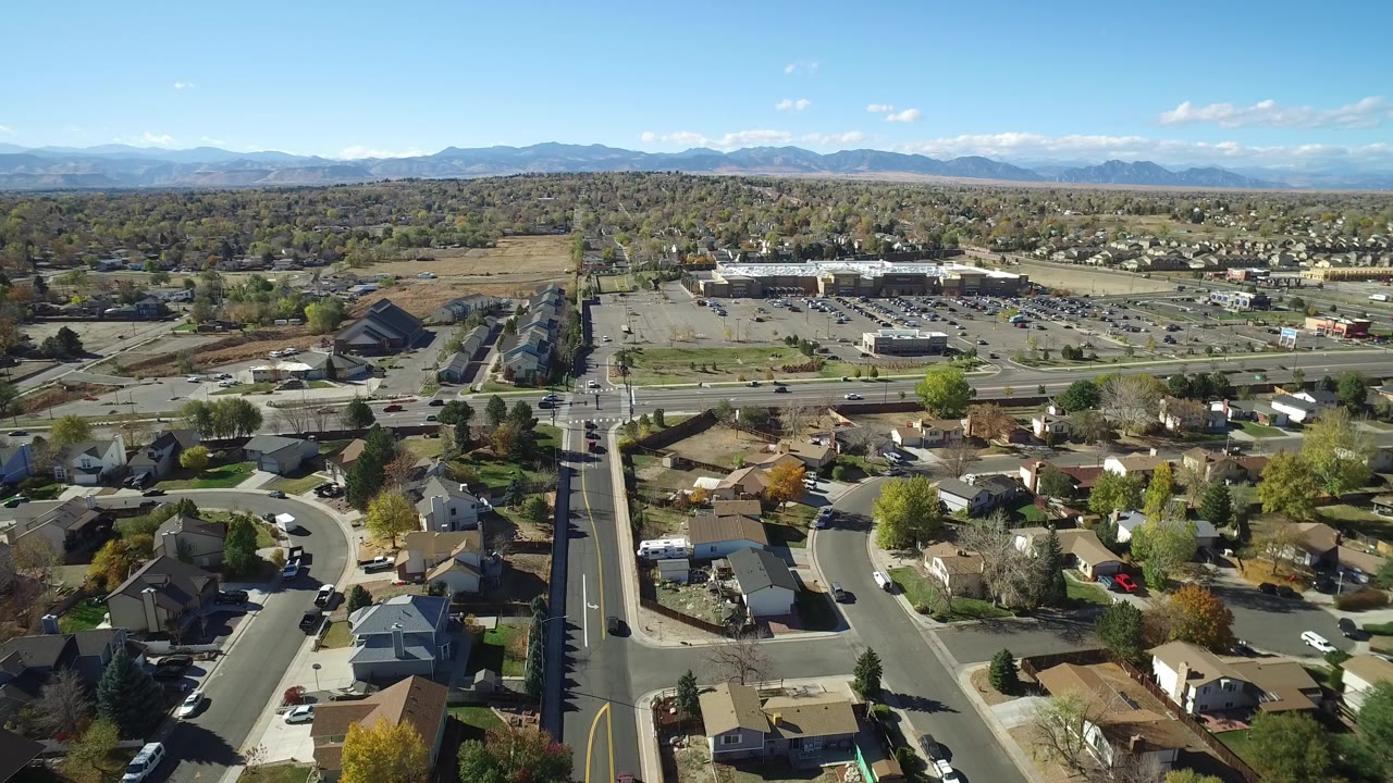 Aerial view over suburban streets, homes, parking lots, and distant mountains.