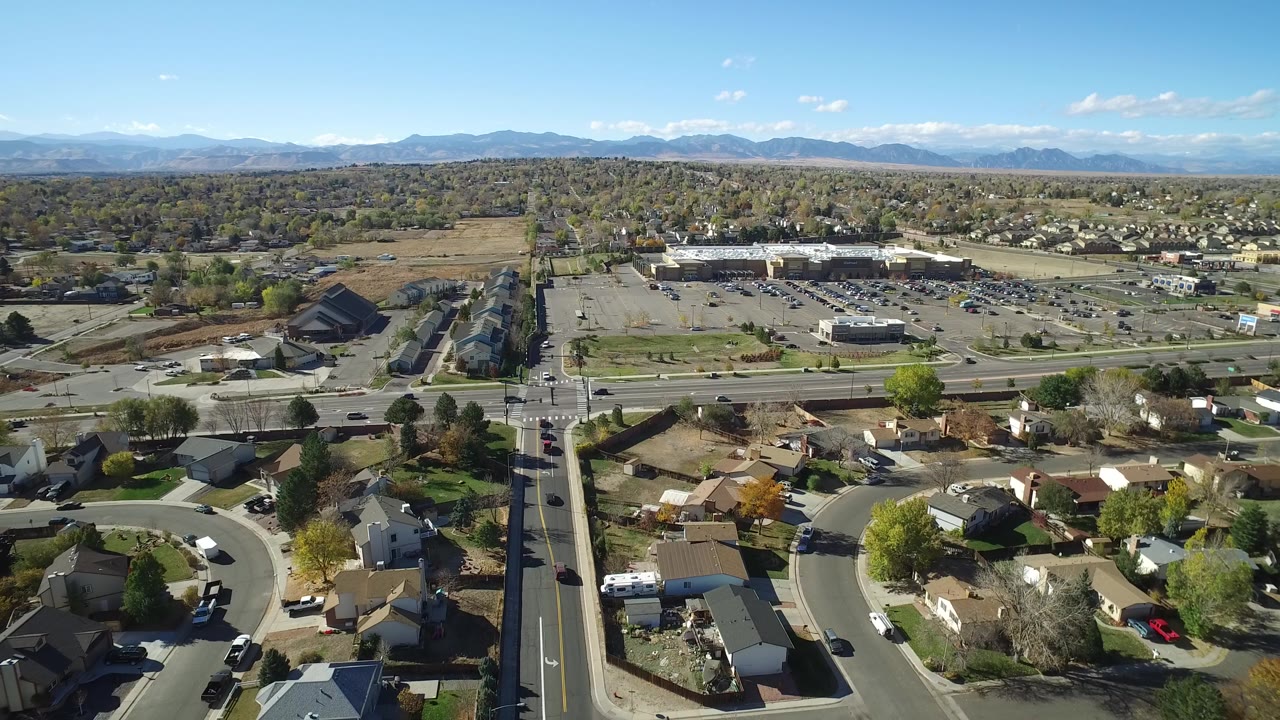 Aerial view over suburban homes, roads, parking lots, trees, and distant mountains.