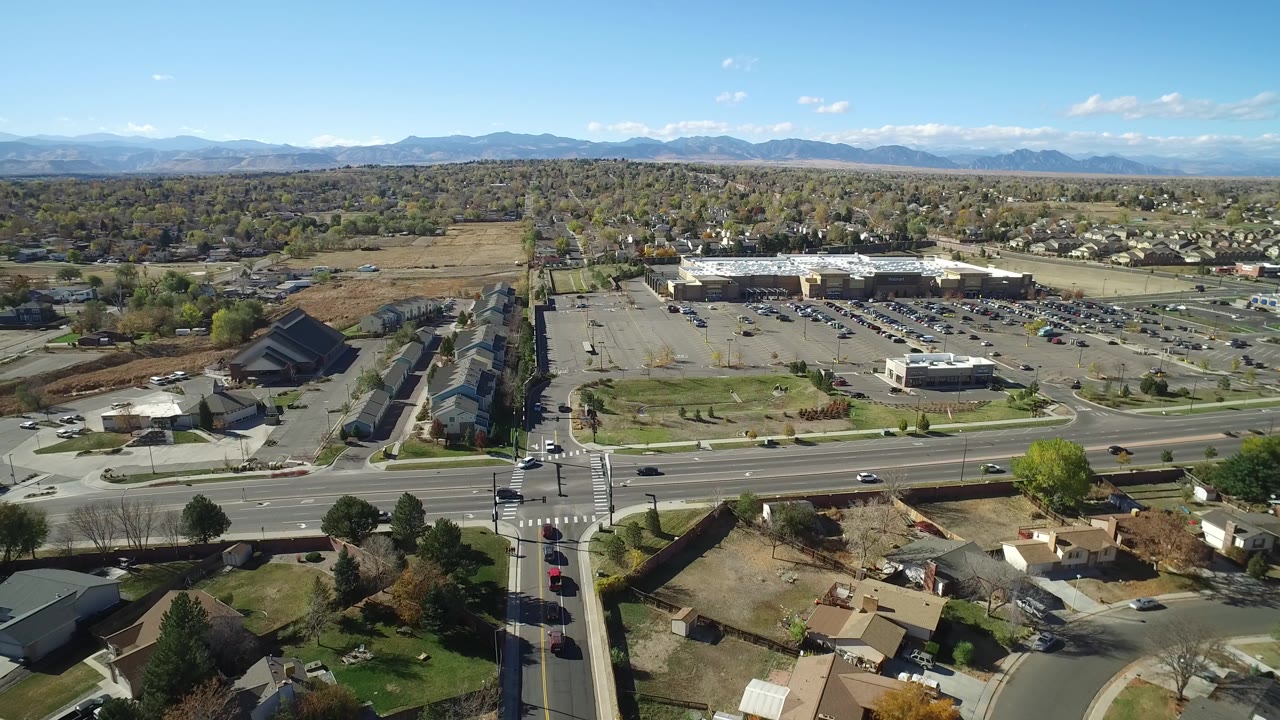 Aerial view of a suburban road, parking lots, homes, and distant mountains.