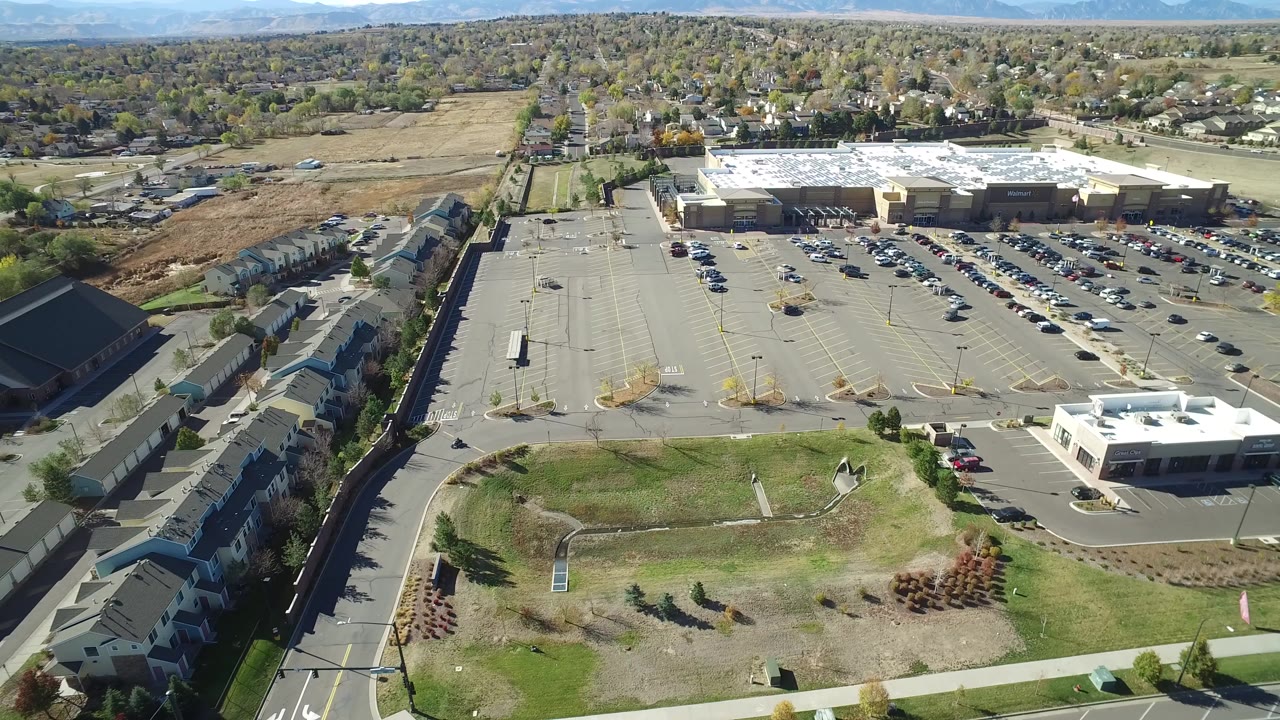 Aerial view over a shopping center parking lot and nearby homes.