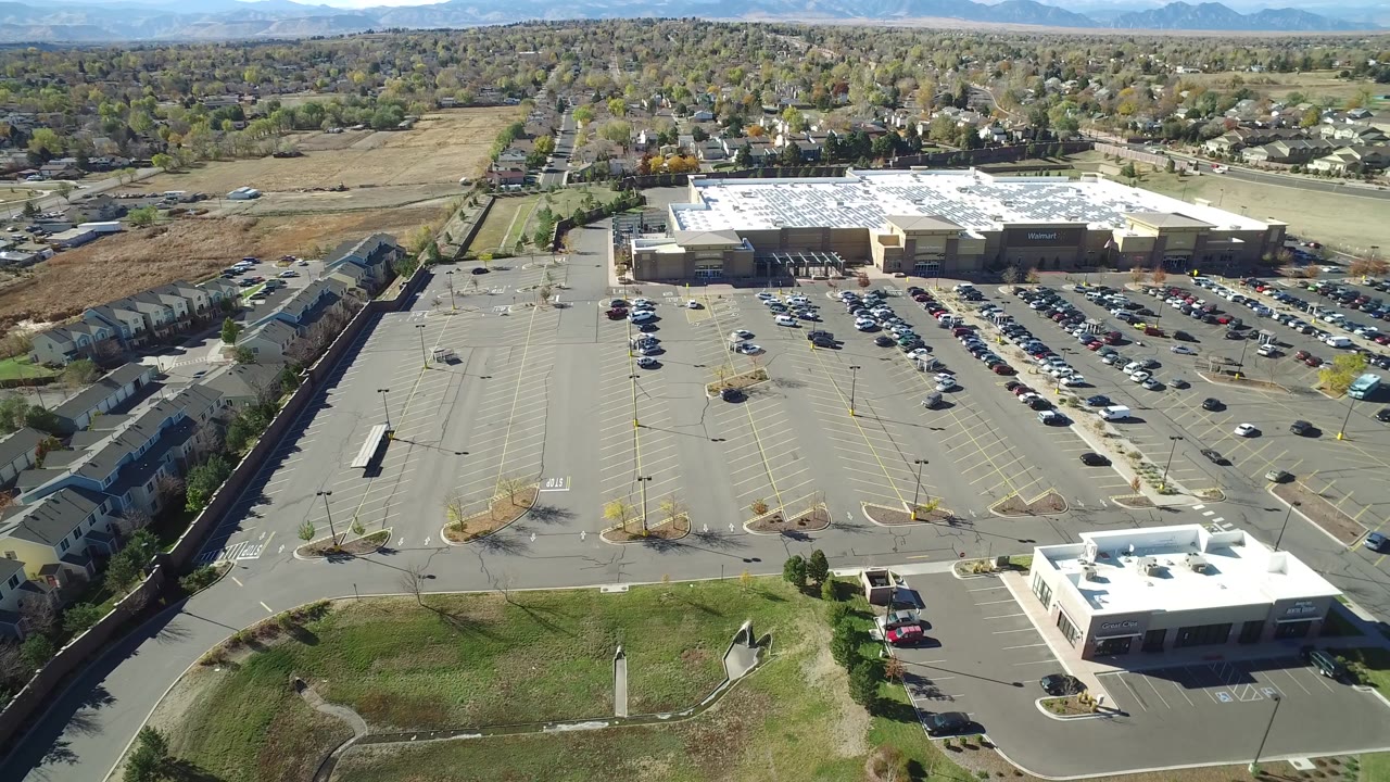 High aerial of a busy shopping center parking lot under bright sun.