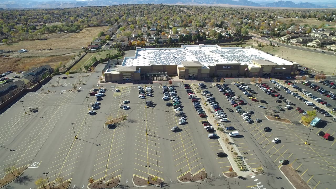 Aerial view of a large retail parking lot with rows of cars and a tan building.