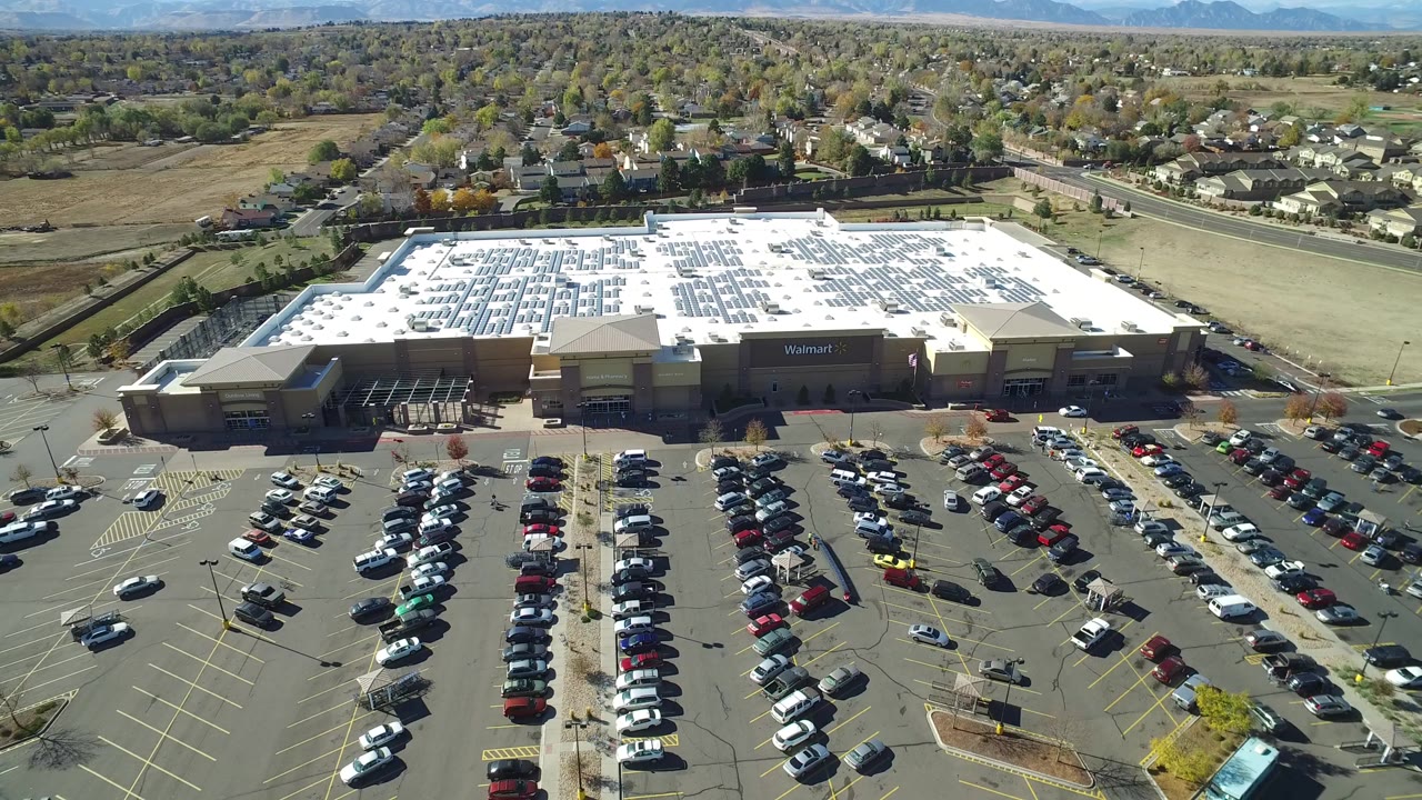 High aerial view of a Walmart parking lot with many parked cars and neighborhoods beyond.