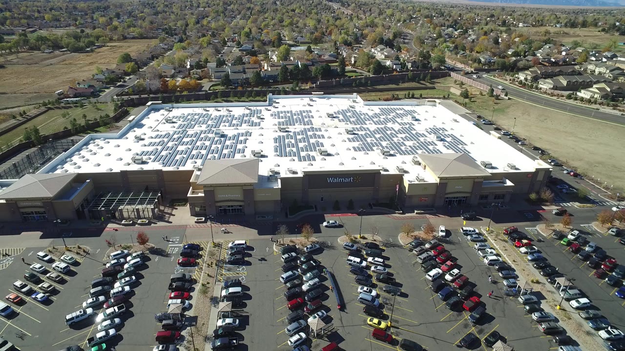 Aerial frame from Hidden Lake, Colorado with the store roof centered, rows of cars in the foreground, and a road and neighborhood behind the retail site.