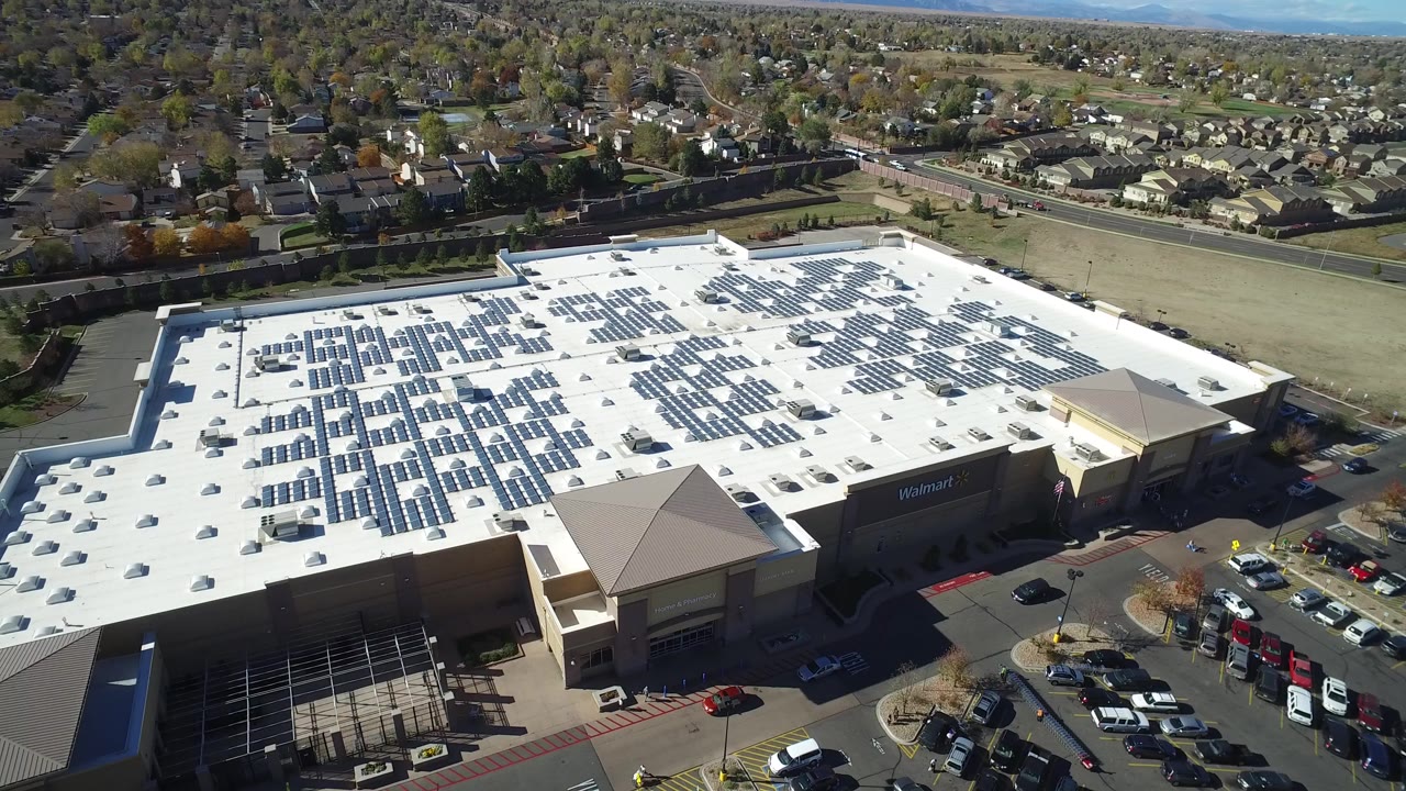 High drone view of a large store roof with solar panels and surrounding parking lots.