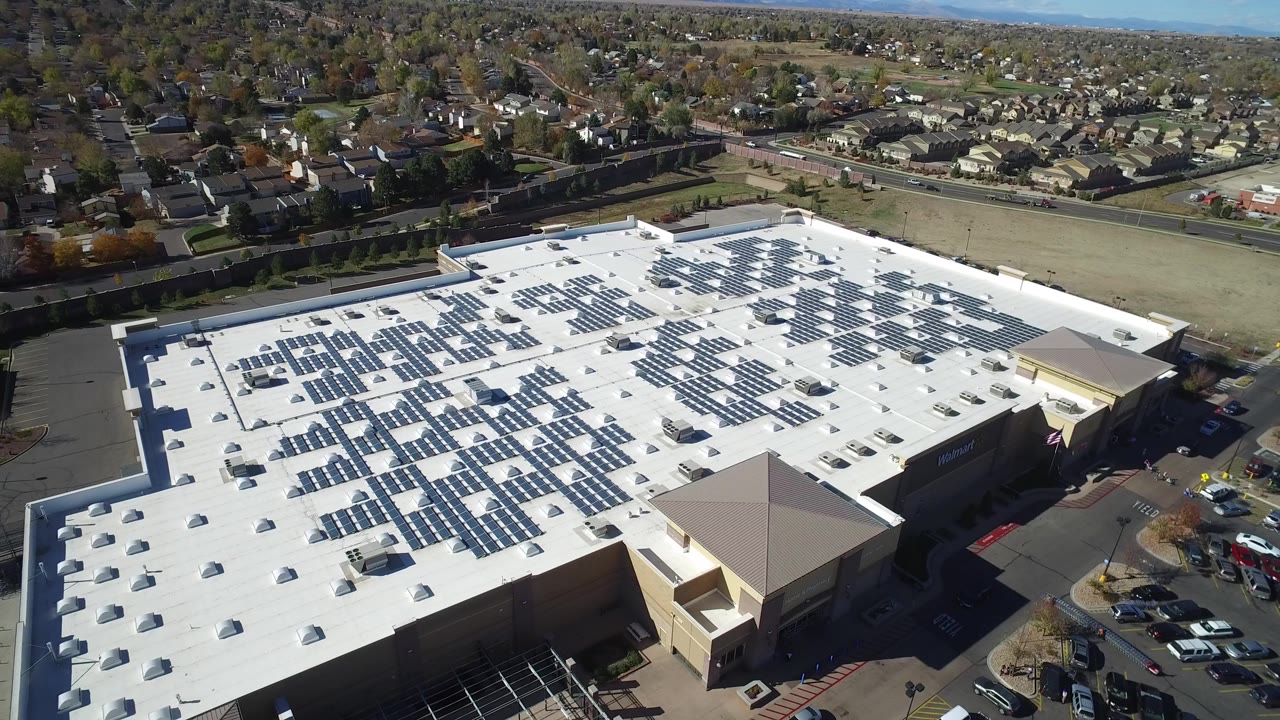 Aerial view of a white-roofed commercial building covered with solar panels.